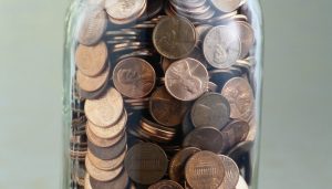 This image shows a transparent cup or mason jar, filled with pennies.